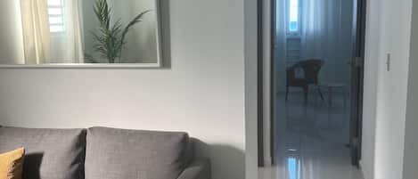 Ein modernes Wohnzimmer mit einem grauen Sofa, einem großen Spiegel und Blick in einen anderen Raum durch eine offene Tür.