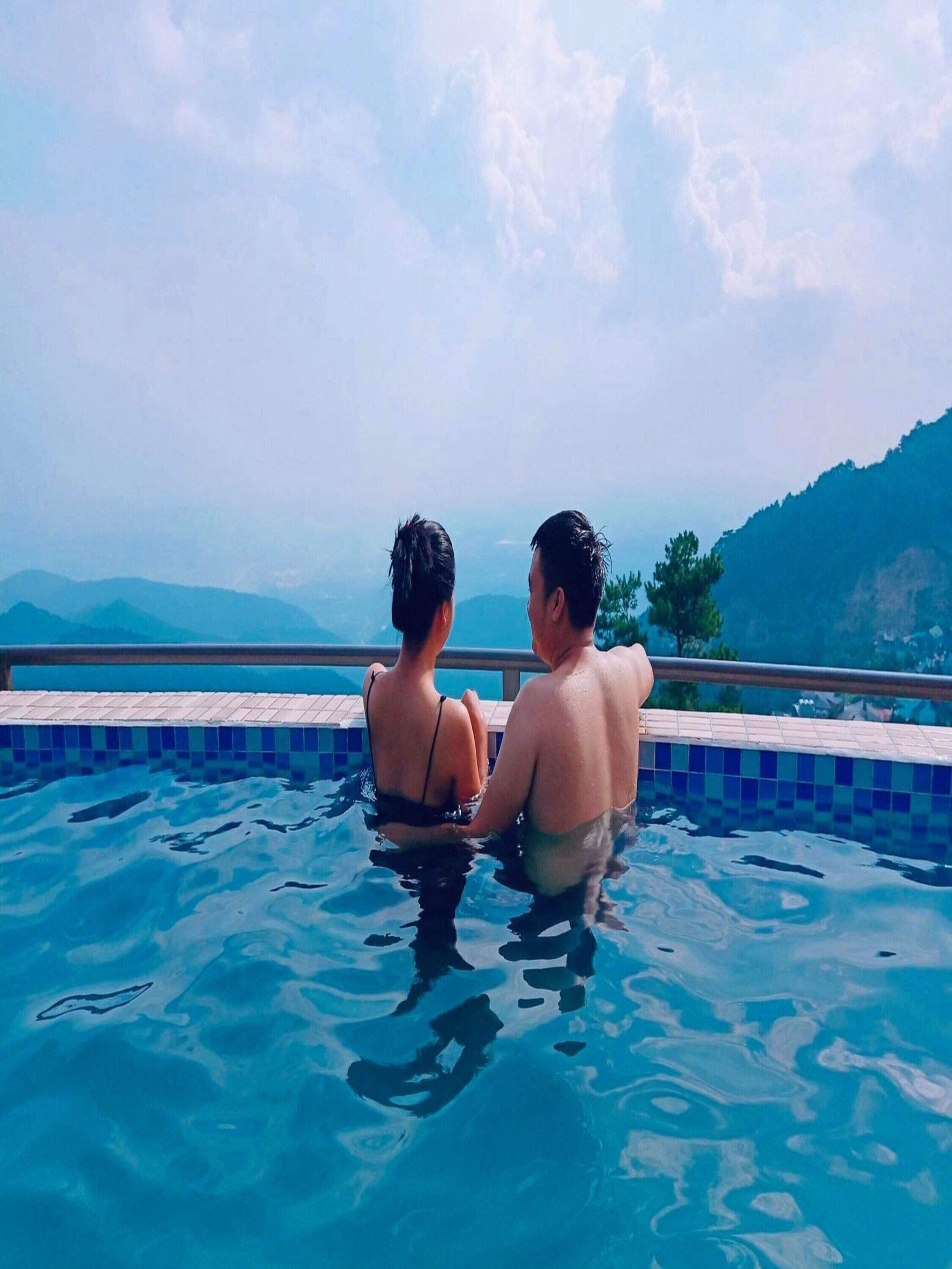 Deux personnes sont assises au bord d’une piscine, avec une vue sur les montagnes.