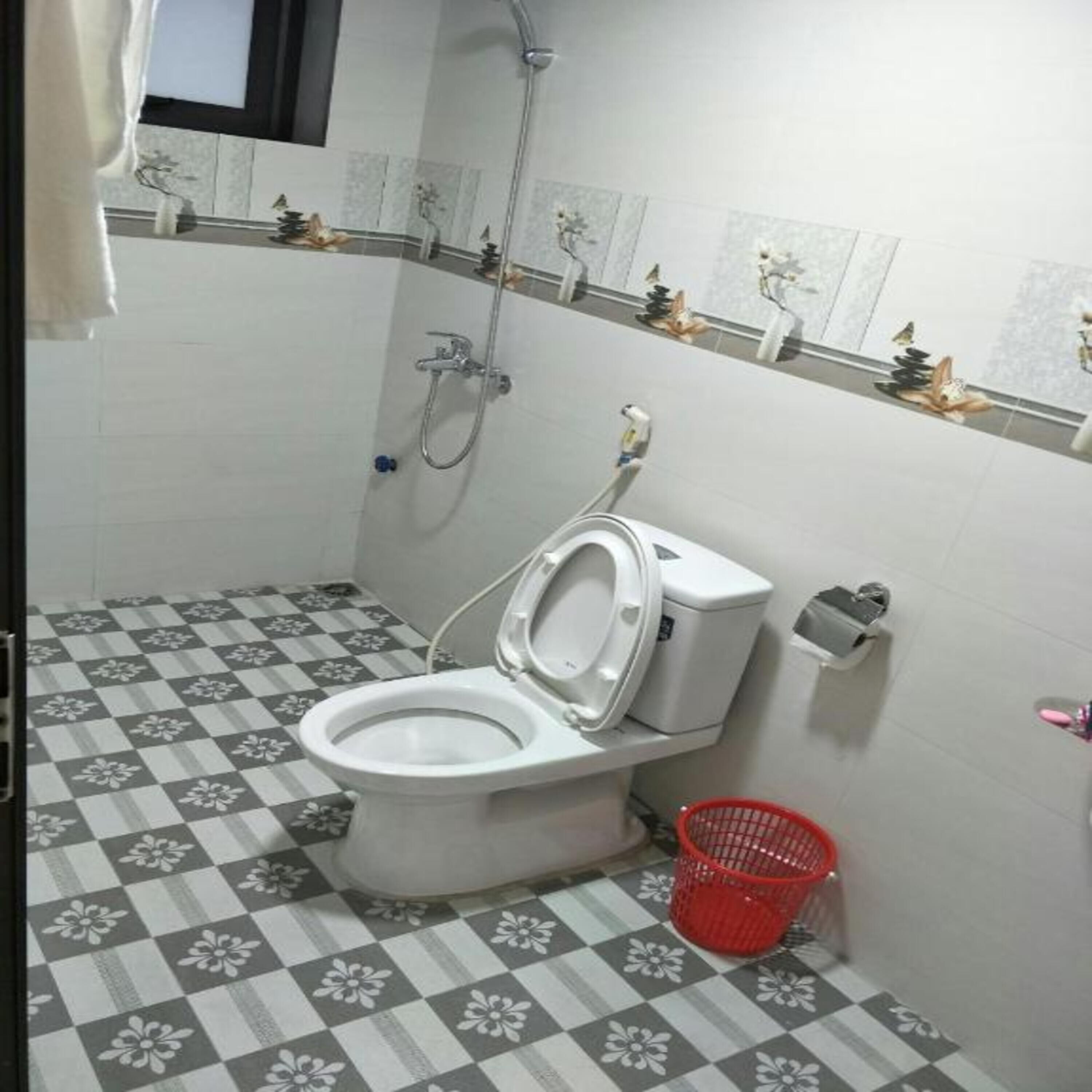 Casa de banho com sanita, chuveiro e um contentor de lixo vermelho.