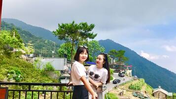 A balcony with a view of a mountainous landscape, a road with vehicles, and some greenery.