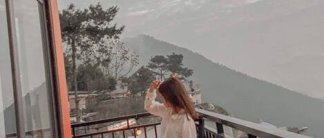 Une personne assise sur un balcon, avec vue sur une montagne et des arbres.