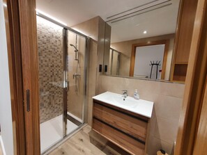A modern bathroom with a glass-enclosed shower, a white sink, and wooden cabinetry.