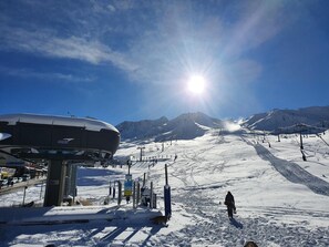 A ski resort with a large snow-covered mountain in the background, a ski lift, and a person skiing down the slope.