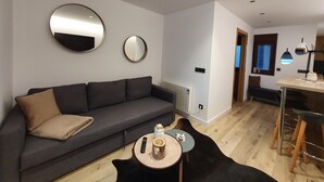 A modern living room with a grey sofa, two round mirrors, a small round table with a remote control, a candle, and a wooden bowl.