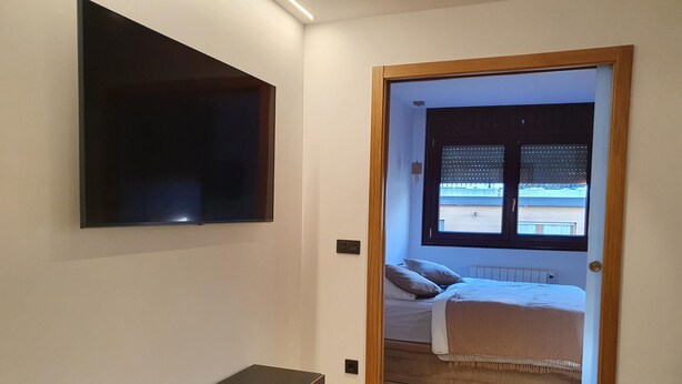 A modern bedroom with a bed, a TV mounted on the wall, and a small table with decorative items.