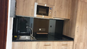 A kitchen with wooden cabinets, a stainless steel microwave, a black countertop, and a sink.