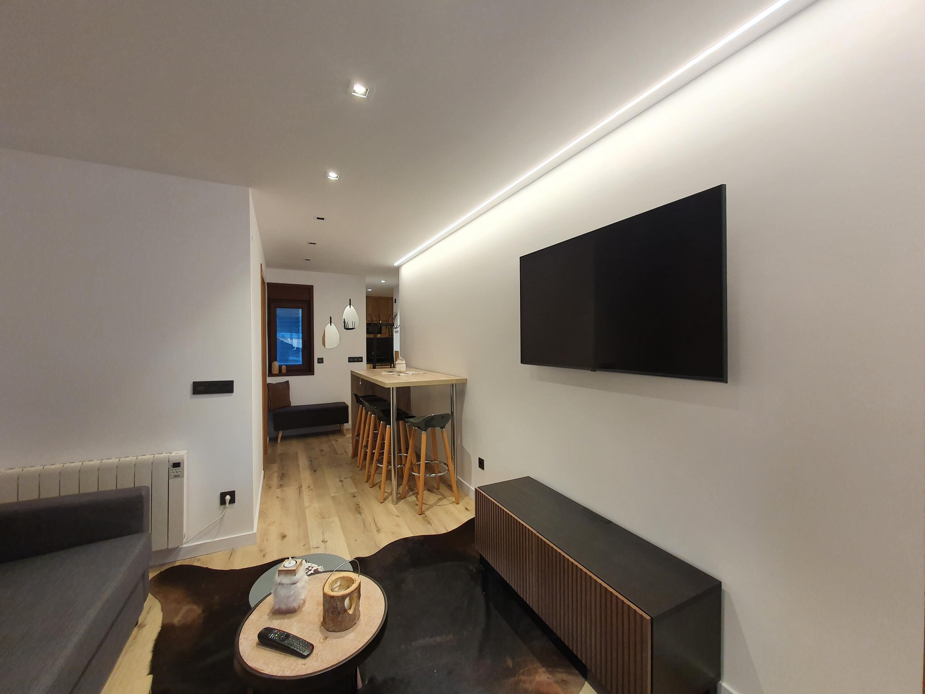Ett modernt vardagsrum med en soffa, ett soffbord, en TV som är monterad på väggen och en matplats med ett bord och stolar.