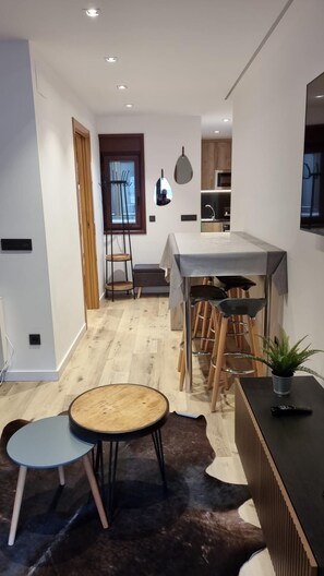 A modern kitchen with a central island, wooden stools, a dining table, and a potted plant.