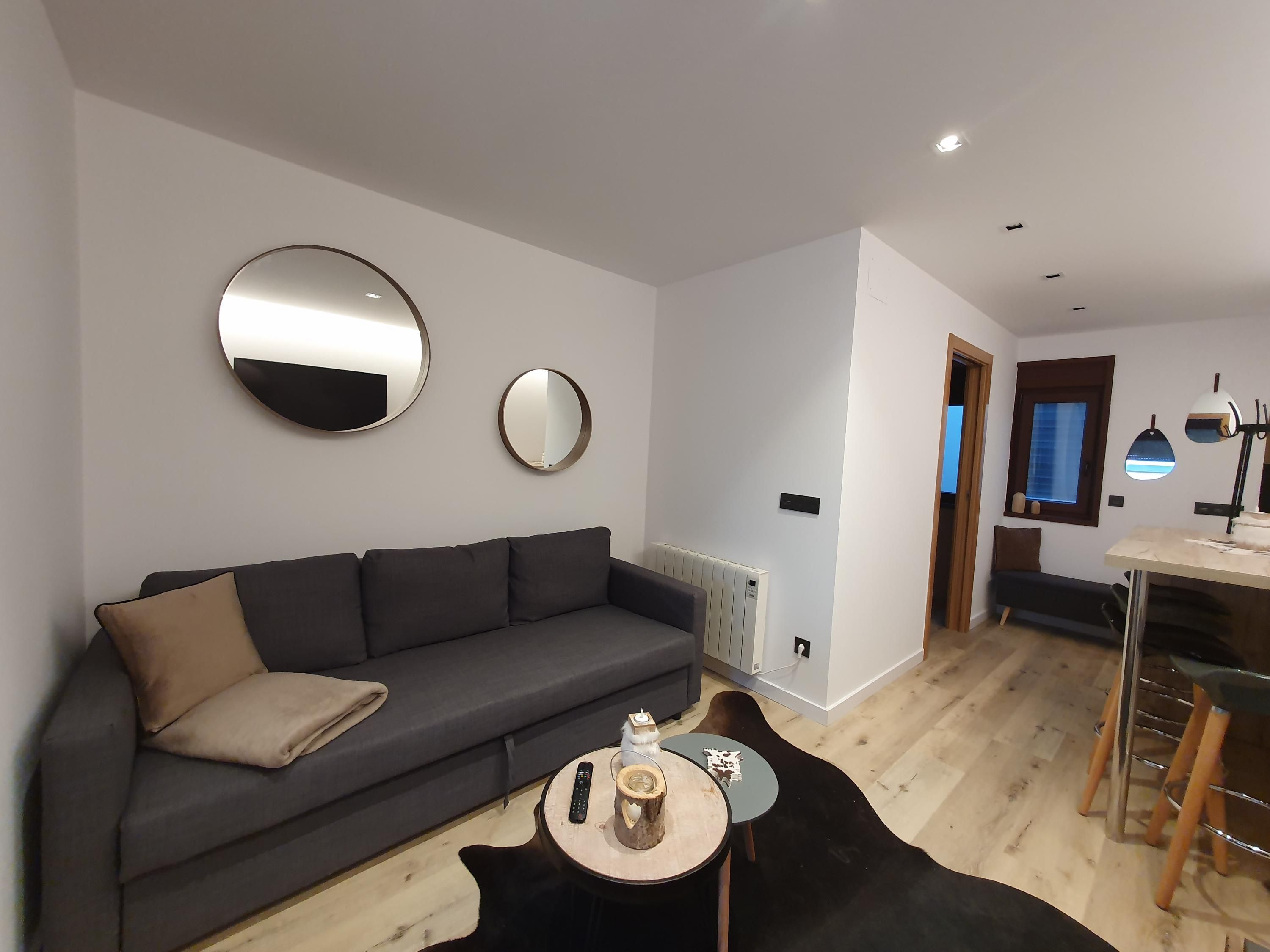Una sala de estar moderna con un sofá gris oscuro, una mesa de centro redonda y una alfombra negra.