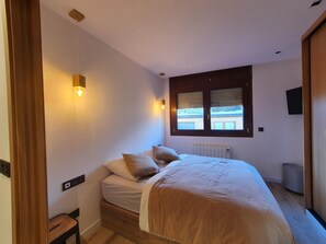 A bedroom with a bed, bedside lamps, a window, and a radiator.