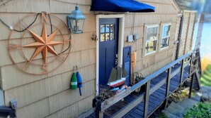 Una casa in legno con una porta blu, una bussola grande appesa al muro e un piccolo portico con tenda blu.