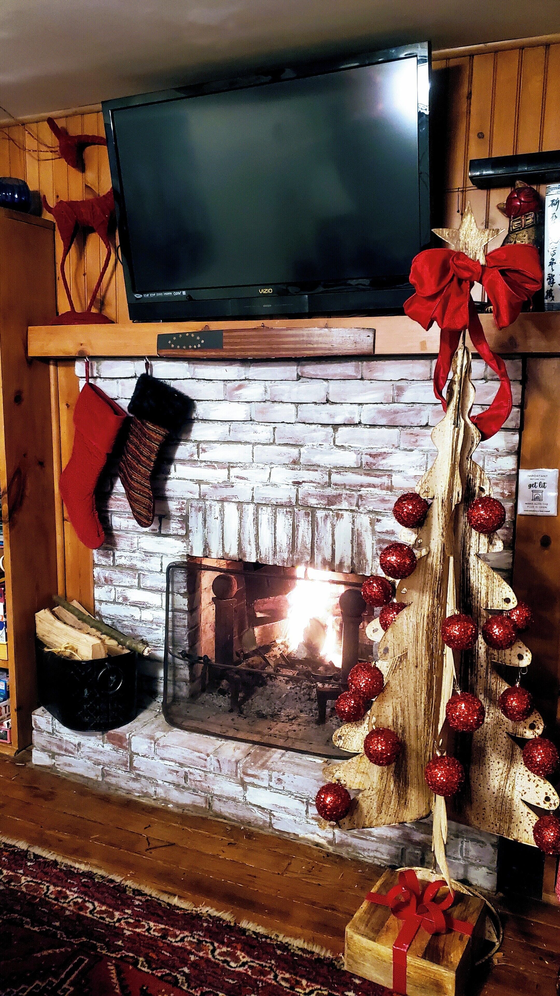 A fireplace with a TV above it, a Christmas tree with red ornaments, and a red bow.
