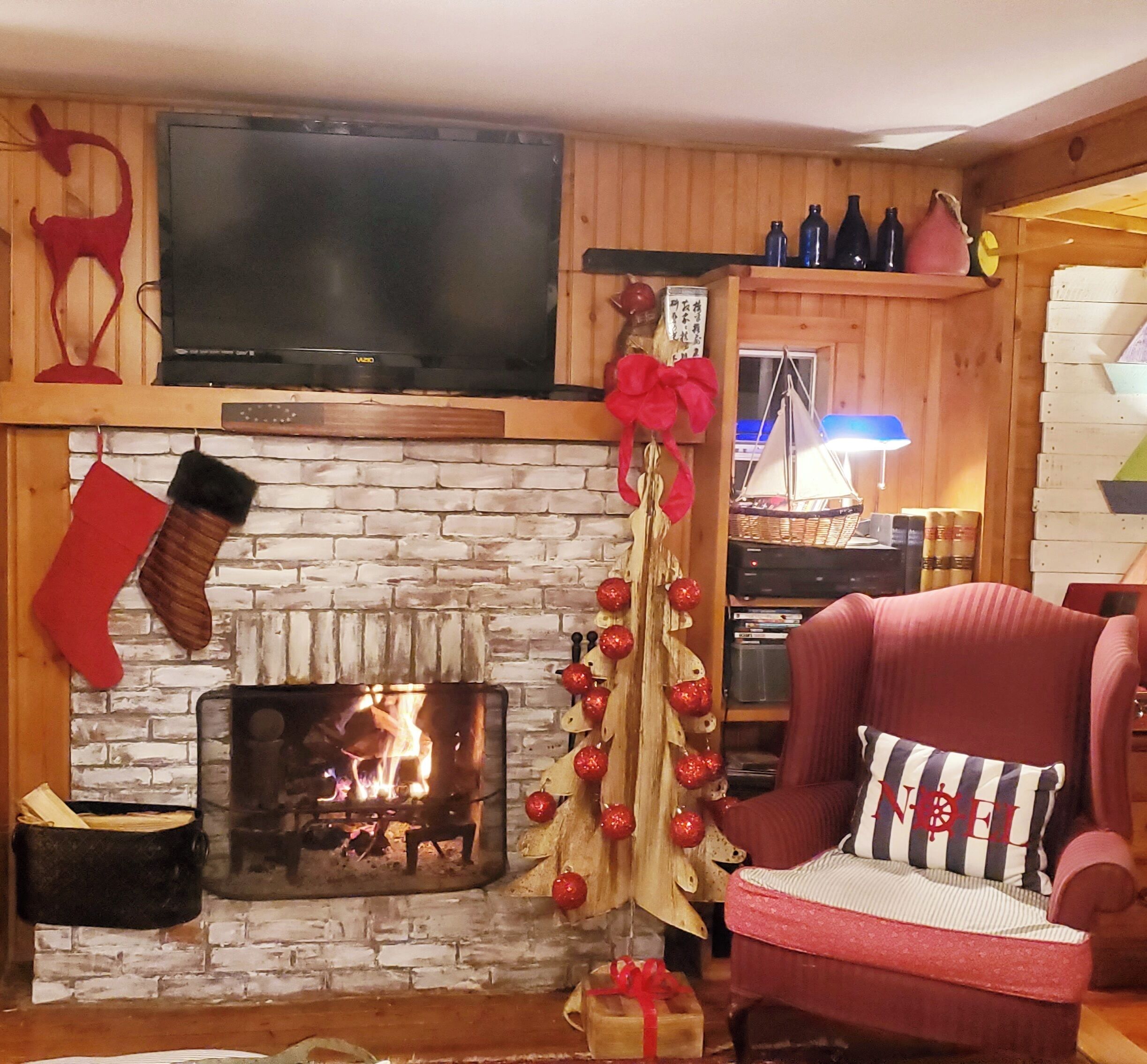 Un salon chaleureux avec une cheminée, un téléviseur fixé au-dessus et un sapin de Noël décoré.