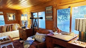 L'interno accogliente di una baita con un'ampia finestra, un telescopio, un cartello con la scritta 'Regole del Lago' e un divano confortevole.