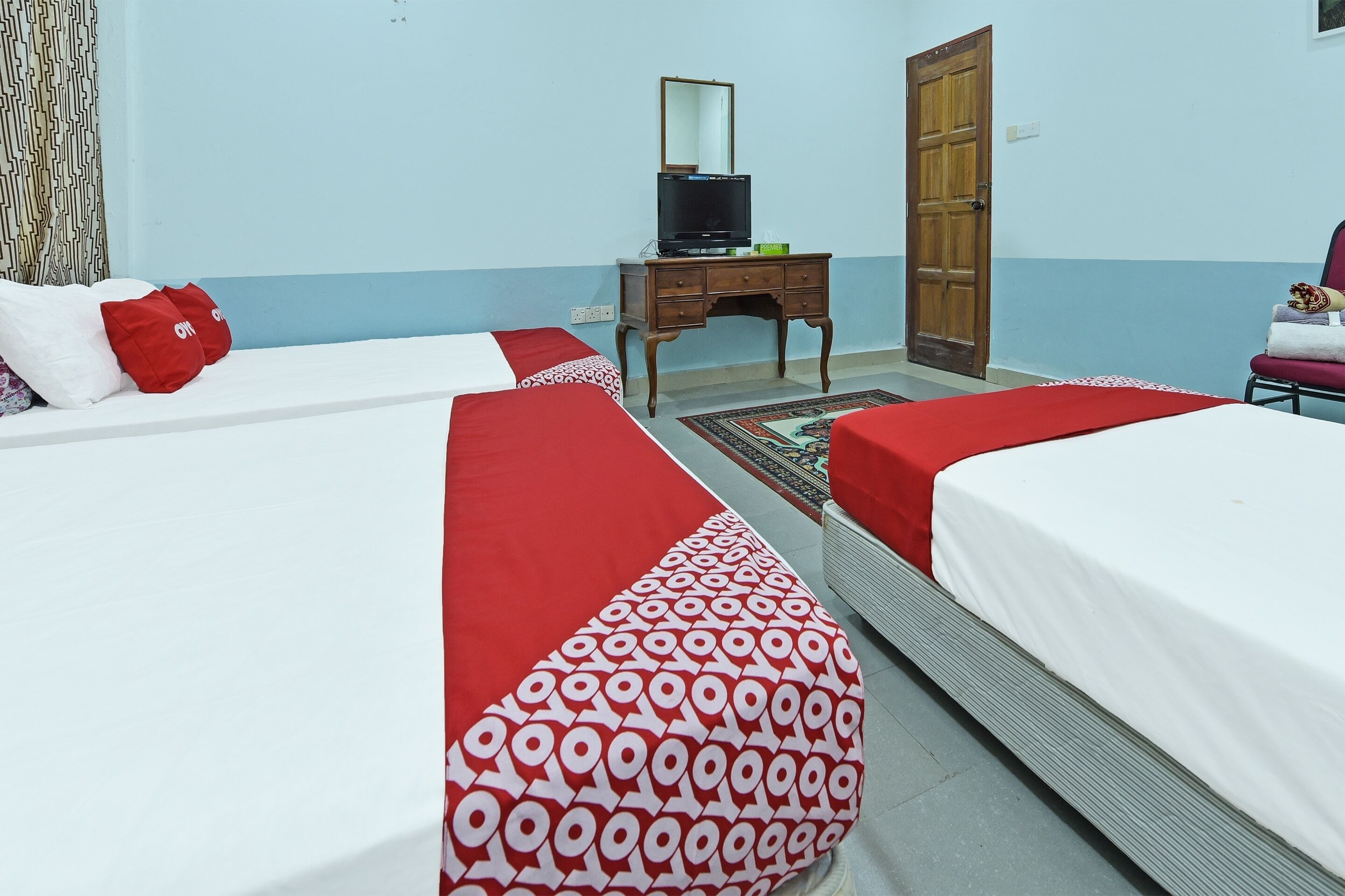 A hotel room with two beds, a wooden dresser, a television, and a mirror.