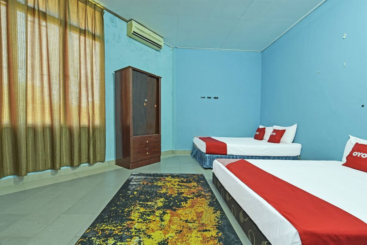 A hotel room with two beds, a wardrobe, and a large window with curtains.