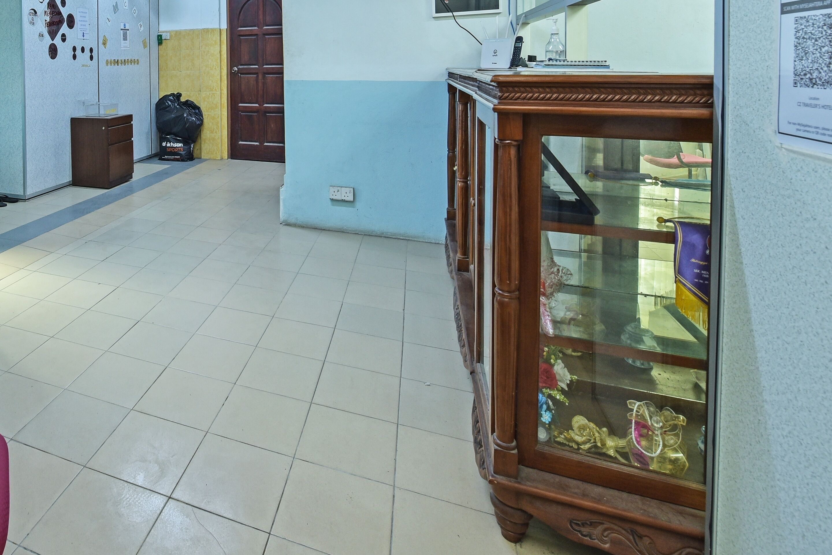 A hallway with a wooden cabinet displaying various items, a trash bin, and a door.