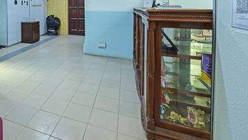 A hallway with a wooden cabinet displaying various items, a trash bin, and a door.