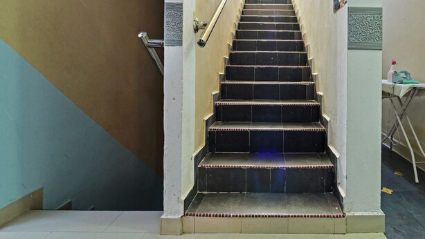 A staircase with black steps and a beige handrail, leading to a landing with a light-colored wall and a decorative panel.