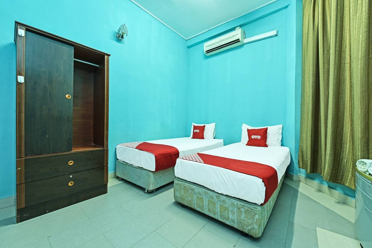 A room with two beds, a wardrobe, and an air conditioning unit.