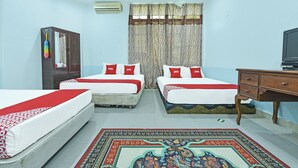 A hotel room with two beds, a wooden wardrobe, a television, and a patterned rug.