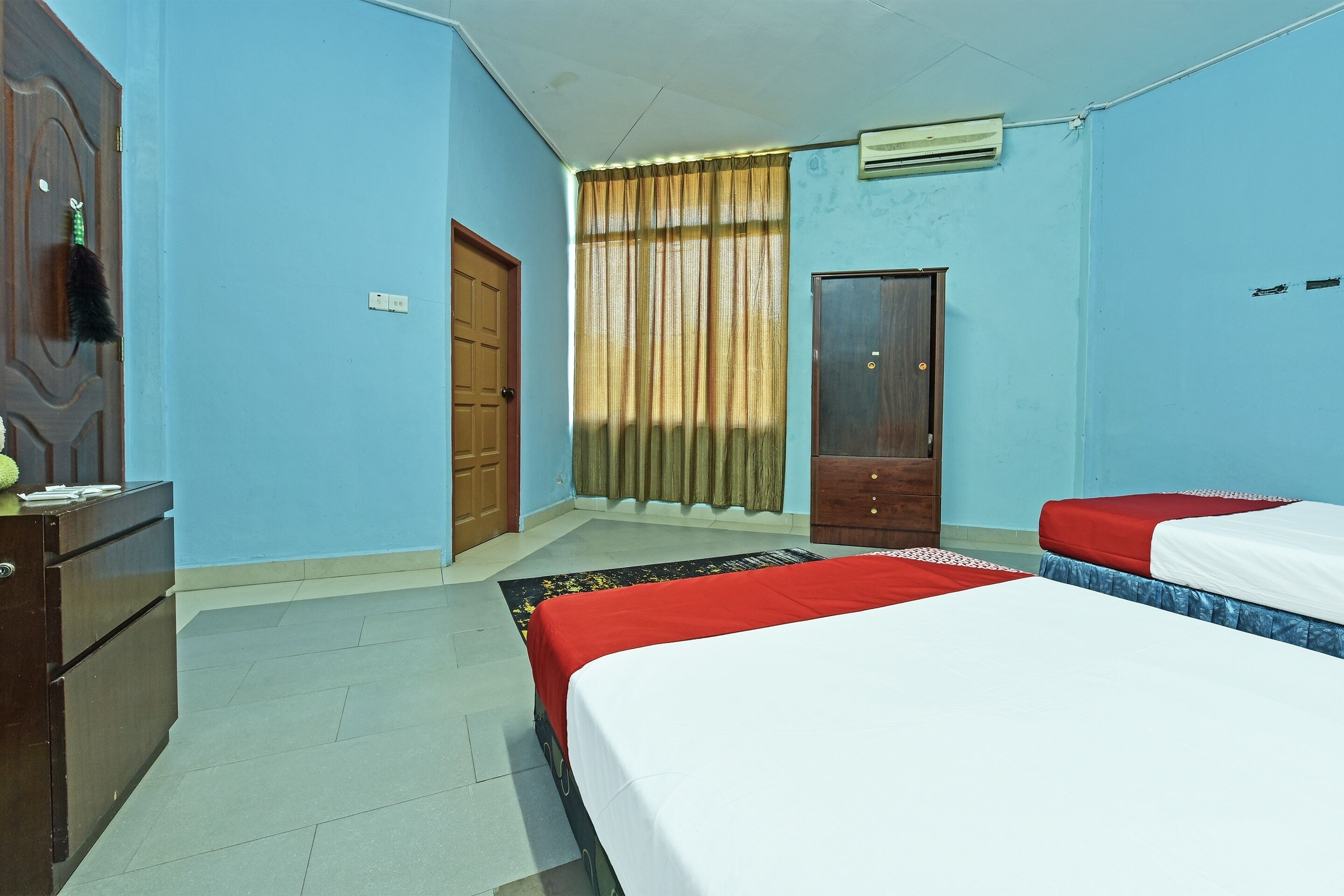 A hotel room with two beds, a wooden dresser, a wardrobe, and a window with curtains.