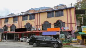 A multi-story building with a yellow facade, a sign for 'WISMA TUAH HOTEL', and a parked black car in front.