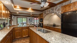 A spacious kitchen with granite countertops, wooden cabinets, a stone accent wall, and a black refrigerator. - Mountain House Hot Tub Pool Table Fire Pit Private beach Walkable to the Lake. (Lake Harmony)
