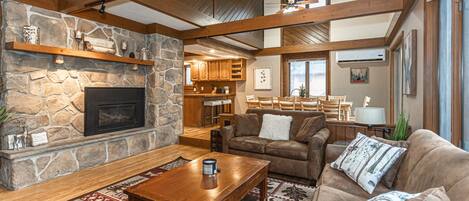 A cozy living room with a stone fireplace, wooden beams, a sofa, and a coffee table.