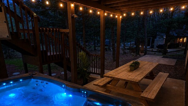 A hot tub with blue lighting, wooden deck, picnic table, and string lights. - Mountain House Hot Tub Pool Table Fire Pit Private beach Walkable to the Lake. (Lake Harmony)