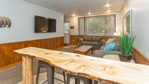 A cozy living area with a wooden bench, a sofa with cushions, a television mounted on the wall, and a window with blinds. - Mountain House Hot Tub Pool Table Fire Pit Private beach Walkable to the Lake. (Lake Harmony)