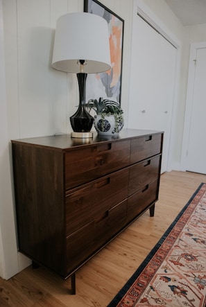 Une commode en bois foncé, surmontée d’une lampe blanche et agrémentée d’un bol décoratif contenant des plantes.