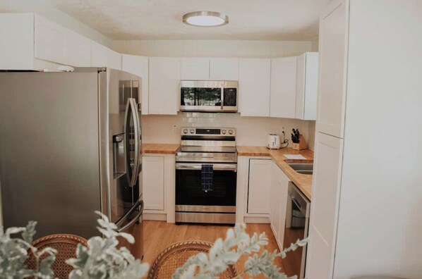 A compact kitchen with a stainless steel refrigerator, microwave, and oven, wooden countertops, and white cabinetry. - Star Valley Ranch, WY Golf Course Home - 8 Beds, Tesla Charger, Near Jackson (Star Valley Ranch)