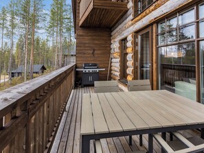 A wooden deck with a grill and seating area, overlooking a forested landscape.