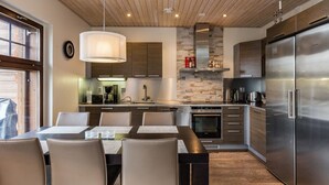 Een moderne keuken met een centraal kookeiland, roestvrijstalen apparatuur en een eethoek met stoelen en een tafel.