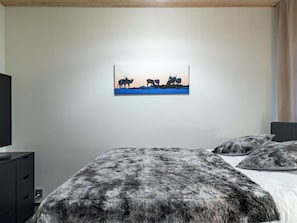 Un dormitorio con una cama, un televisor y un cuadro de renos en la pared.