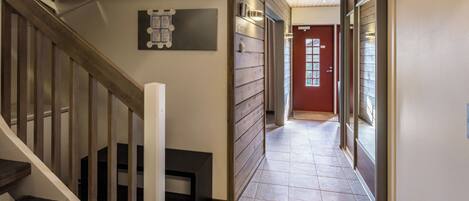 A hallway with a wooden staircase, a red door, and a tiled floor.