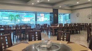 A spacious restaurant with multiple tables and chairs, large windows offering a view of the outside, and a modern ceiling design with recessed lighting. - Rylich Panorama Hotel (Sorong)