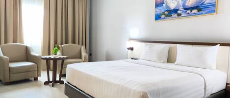 Habitación de hotel con una cama grande, dos sillones, una mesita con una planta y un cuadro de cisnes en la pared.