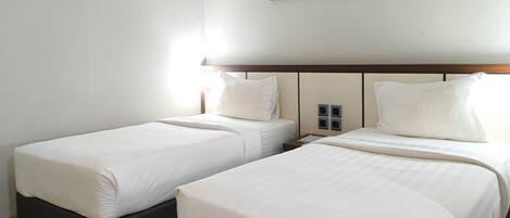 Habitación de hotel con dos camas individuales, cabecera de madera, un cuadro de flores en la pared y una mesita de noche con lámpara.