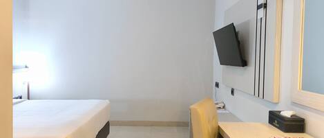 A hotel room with a bed, a desk, a chair, a TV mounted on the wall, and a mirror.