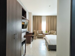 A hotel room with a bed, two armchairs, a desk with a TV, and a minibar.