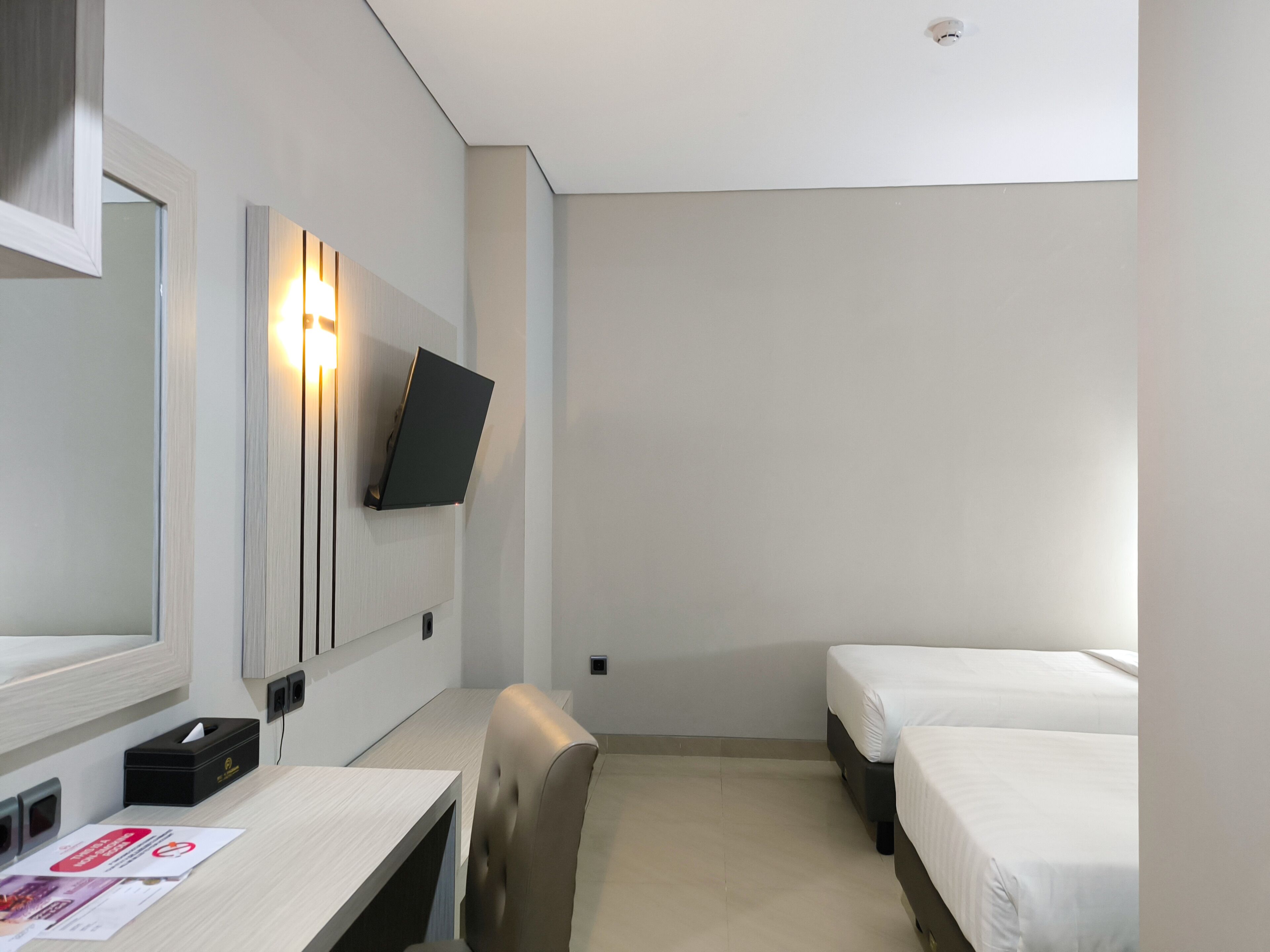 A hotel room with a desk, chair, two beds, a TV mounted on the wall, and a mirror.