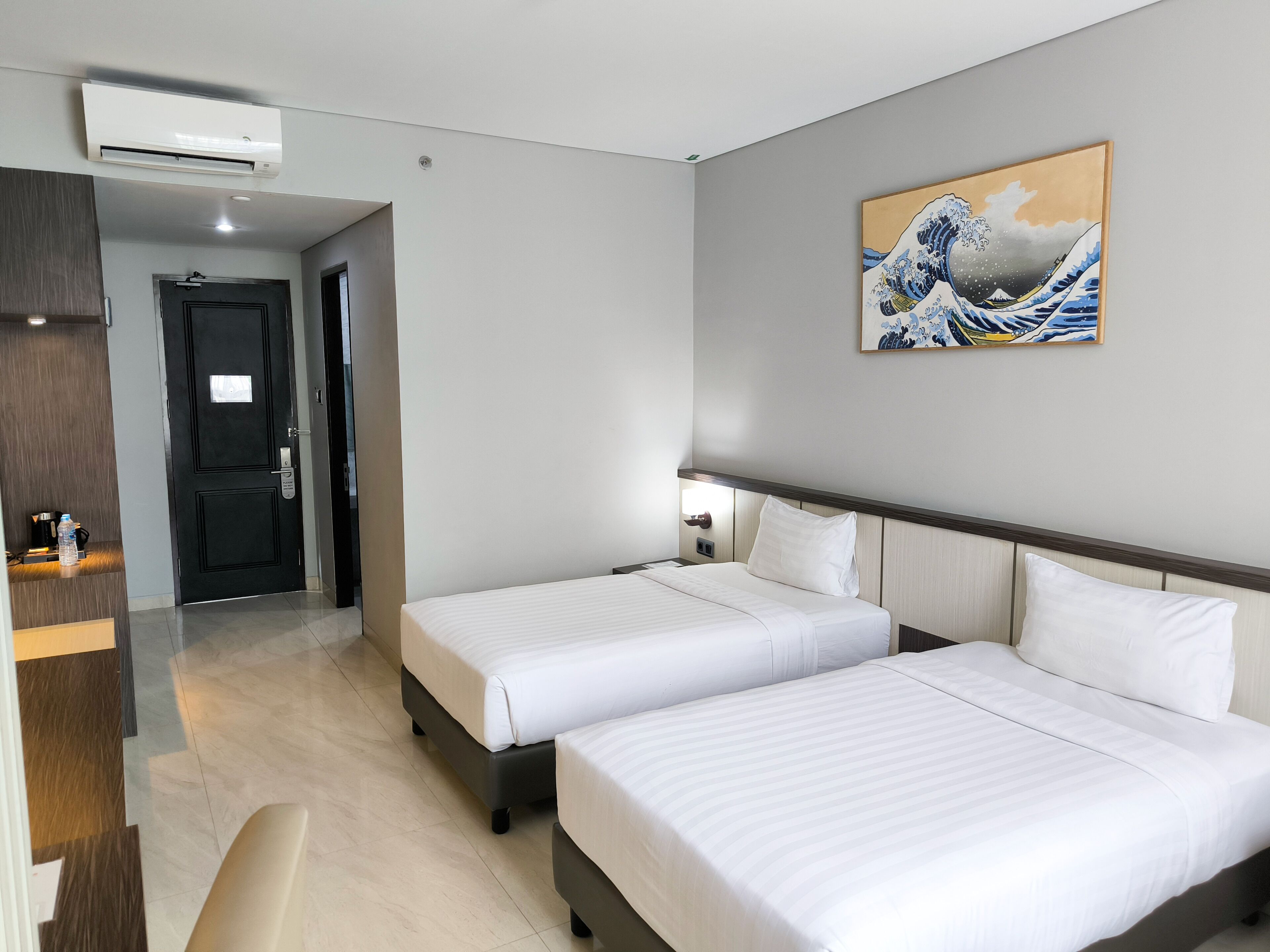 A hotel room with two beds, a desk, and a painting on the wall.
