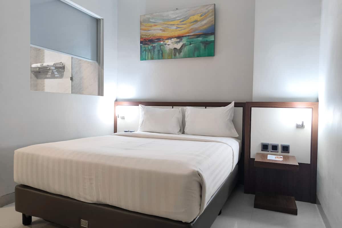 A neatly made bed with a wooden headboard, a bedside table with a lamp, and a painting on the wall.