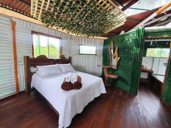 A bedroom with a wooden bed, white linens, and a green wall with a bamboo installation.
