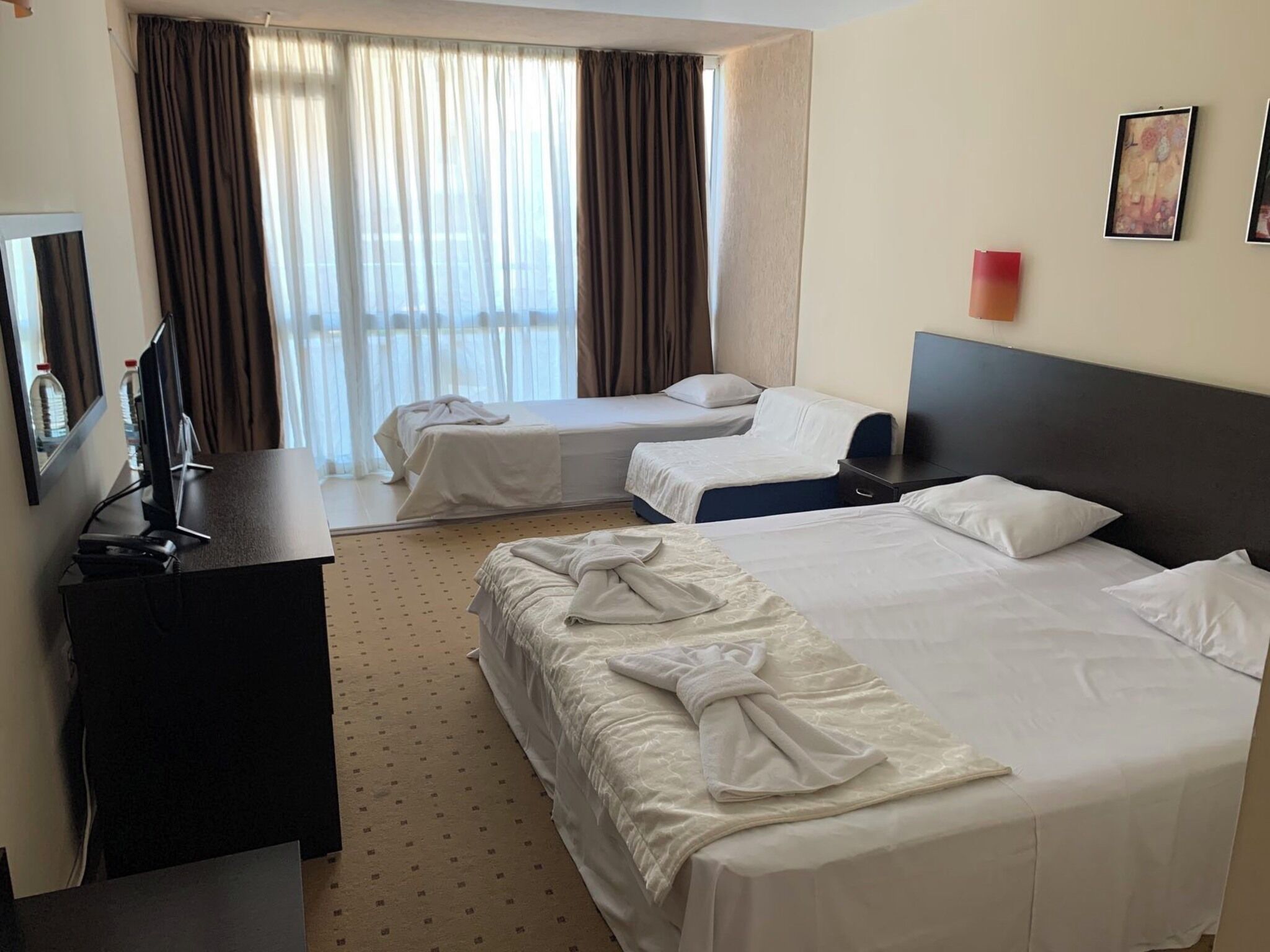 A hotel room with two beds, a desk, a TV, and a window with curtains.