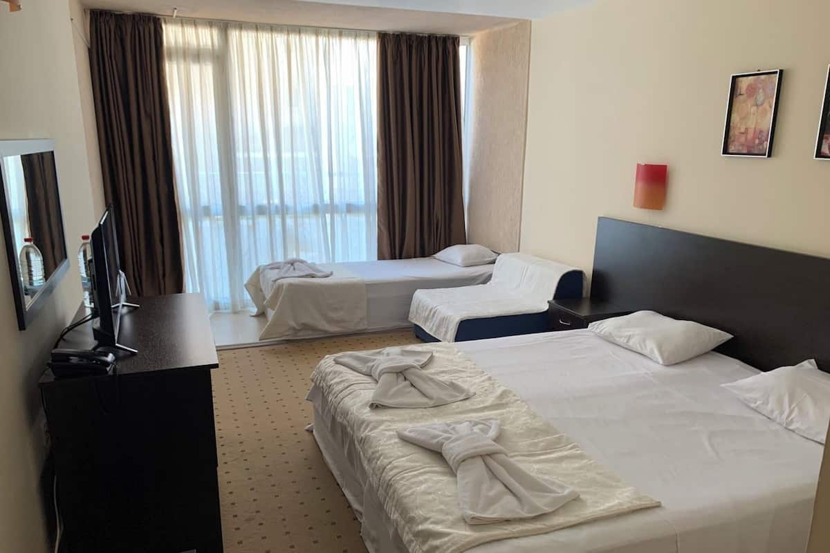 A hotel room with two beds, a desk, a TV, and a window with curtains.
