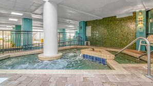 Ein Poolbereich im Innenbereich mit einer zentralen Säule, gefliesten Stufen und einer Wand mit Grüntönen.