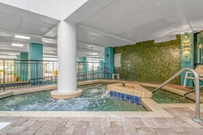 An indoor pool area with a central column, tiled steps, and a green textured wall.